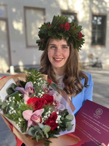Monica neolaureata con corona d’alloro, fiori e pergamena di laurea all’esterno dell’università.